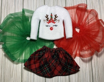 May include: A white Christmas sweater with a reindeer design, a red plaid skirt, and two tulle skirts, one green and one red.