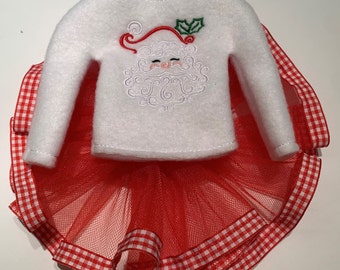 May include: A festive Christmas outfit featuring a white felt sweater with an embroidered Santa Claus face and a red tulle skirt. The skirt is trimmed with a red and white gingham ribbon, creating a holiday-themed ensemble.