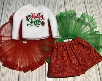 May include: A white sweater with the text "Holly Jolly" embroidered on the front, a red tulle skirt, and a green tulle skirt.