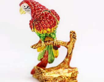 Op de afbeelding: Een rood, groen en geel papegaaibeeldje dat op een gouden tak zit. De papegaai is gemaakt van metaal en heeft een gedetailleerd ontwerp.