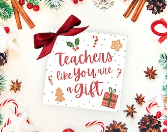 May include: A white card with red and green Christmas decorations and the text "Teachers like you are a gift". The card is surrounded by Christmas decorations, including a red bow, candy canes, and pine branches.