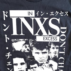 May include: A black short-sleeve t-shirt featuring a white graphic print of the band INXS. The design includes a collage of band members' faces, the text INXS EXCESS, and Japanese characters along with the English text DON'T CHANGE.