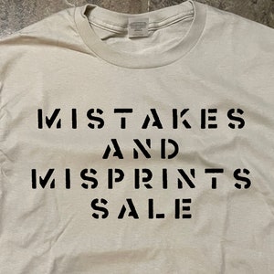May include: A white t-shirt with black text that reads "MISTAKES AND MISPRINTS SALE".