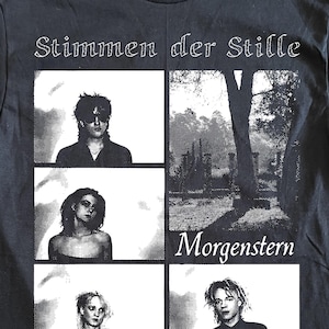 May include: Black t-shirt with the text "Stimmen der Stille" and "Morgenstern" in white. The shirt features a grid design with black and white images of people and a landscape.