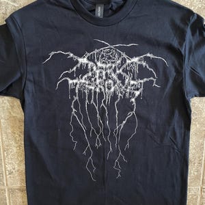 Puede incluir: Camiseta negra con un dise&ntilde;o gr&aacute;fico blanco. El dise&ntilde;o presenta texto estilizado y un pentagrama. La camiseta est&aacute; hecha de un material suave y tiene cuello redondo.