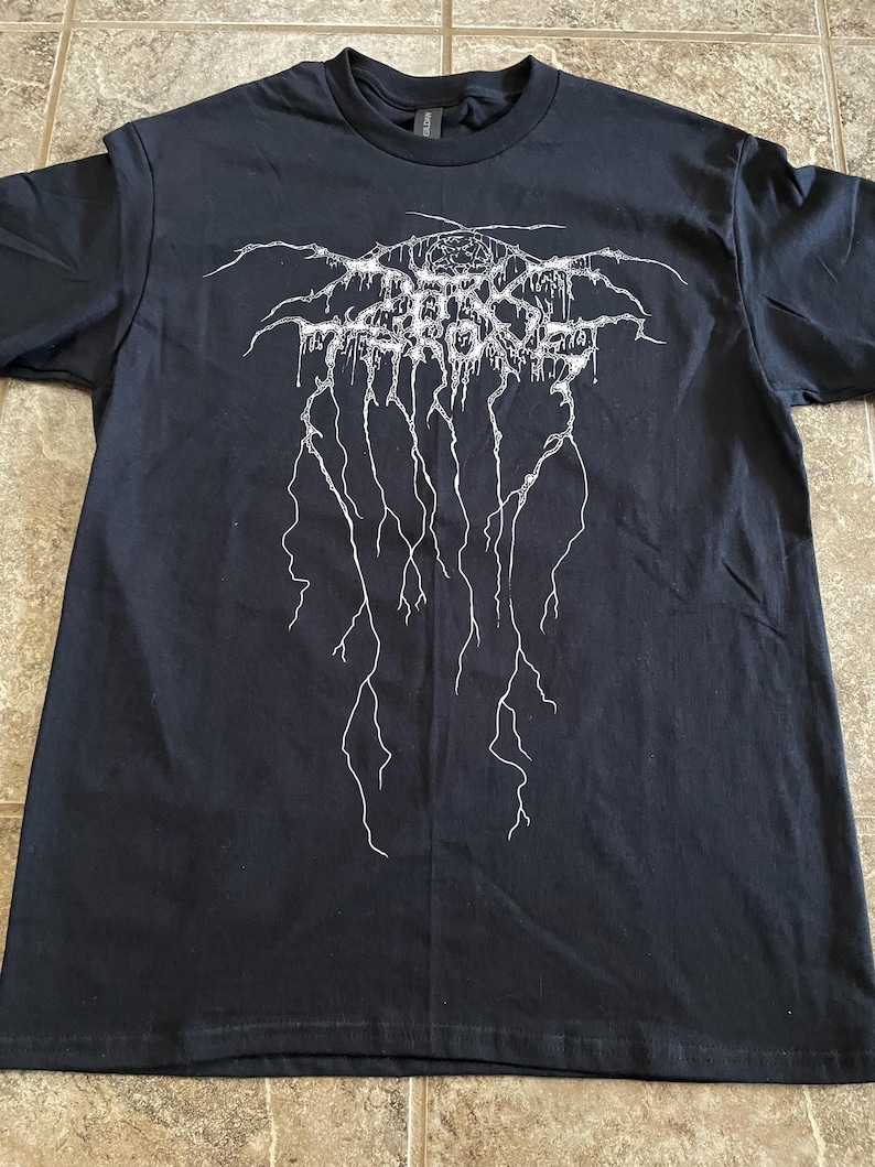 Puede incluir: Camiseta negra con un dise&ntilde;o gr&aacute;fico blanco. El dise&ntilde;o presenta texto estilizado y l&iacute;neas en forma de rayo. La camiseta est&aacute; hecha de un material suave y tiene cuello redondo.