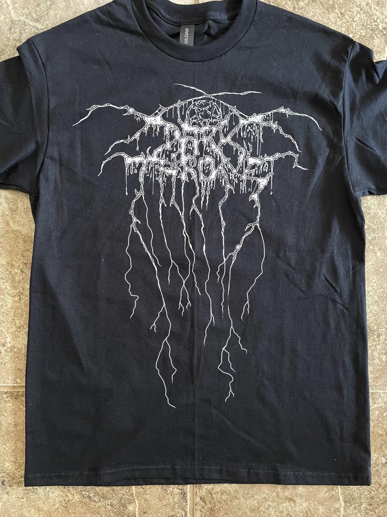 Puede incluir: Camiseta negra con un dise&ntilde;o gr&aacute;fico blanco. El dise&ntilde;o presenta texto estilizado y formas abstractas, con un pentagrama en la parte superior. La camiseta est&aacute; hecha de un material suave y tiene cuello redondo.