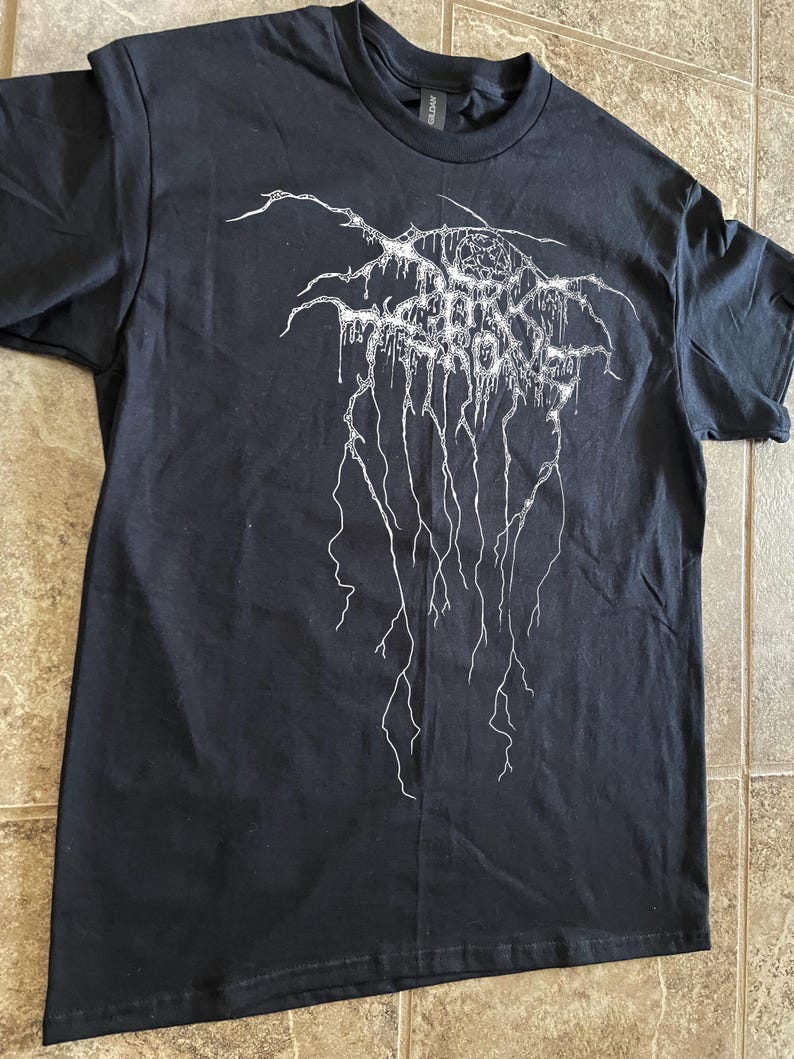 Puede incluir: Camiseta negra con un dise&ntilde;o gr&aacute;fico blanco. El dise&ntilde;o presenta el texto "DARK SORROW" en una fuente estilizada y goteante, con l&iacute;neas ramificadas que se extienden hacia abajo. La camiseta est&aacute; hecha de un material suave.