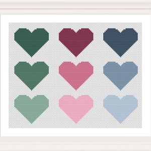 May include: A framed cross-stitch artwork featuring nine pixelated hearts in various colors: dark green, burgundy, navy, medium green, pink, light blue, seafoam green, light pink, and light blue. The hearts are arranged in a 3x3 grid on a light gray background.