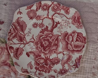 Może przedstawiać: Biały ceramiczny talerz z falistą krawędzią, z czerwonym wzorem kwiatowym. Wzór obejmuje duże róże, mniejsze kwiaty i gałęzie. Talerz ma wygląd vintage i nadaje się do serwowania potraw.