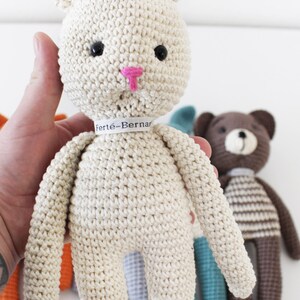 Pode incluir: Um coelho branco de croch&ecirc; com nariz rosa e olhos pretos. O coelho est&aacute; usando uma etiqueta branca com o texto "Fert&eacute;-Bernard".