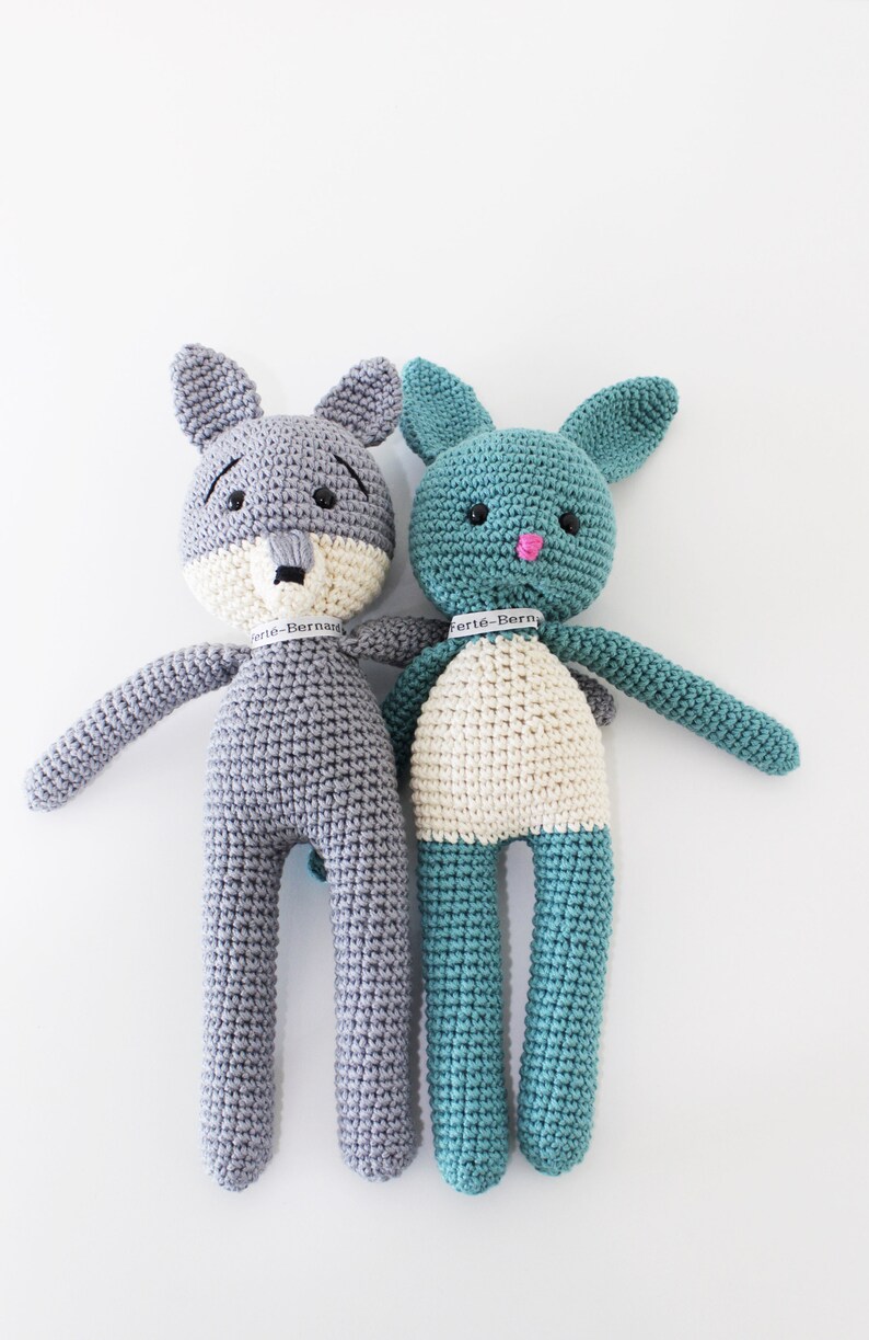 Pode incluir: Dois animais de peluche de croch&ecirc;, um lobo cinza e um coelho azul turquesa, de p&eacute; lado a lado. Ambos t&ecirc;m detalhes brancos e olhos pretos. O lobo tem um focinho branco e o coelho tem um nariz rosa.