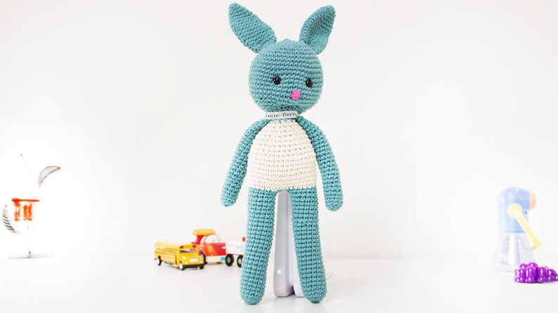 Pode incluir: Um brinquedo de coelho de croch&ecirc; azul com detalhes brancos e nariz rosa. O coelho tem olhos pretos e uma etiqueta branca ao redor do pesco&ccedil;o que diz "Cute Bunny".