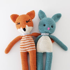 Pode incluir: Dois animais de peluche de croch&ecirc;, uma raposa e um coelho, de p&eacute; lado a lado. A raposa &eacute; laranja com listras brancas e o coelho &eacute; azul turquesa. Ambos t&ecirc;m olhos pretos e narizes cor-de-rosa. A raposa tem uma etiqueta que diz "Berte-Bernard" e o coelho tem uma etiqueta que diz "Berte-Bern".