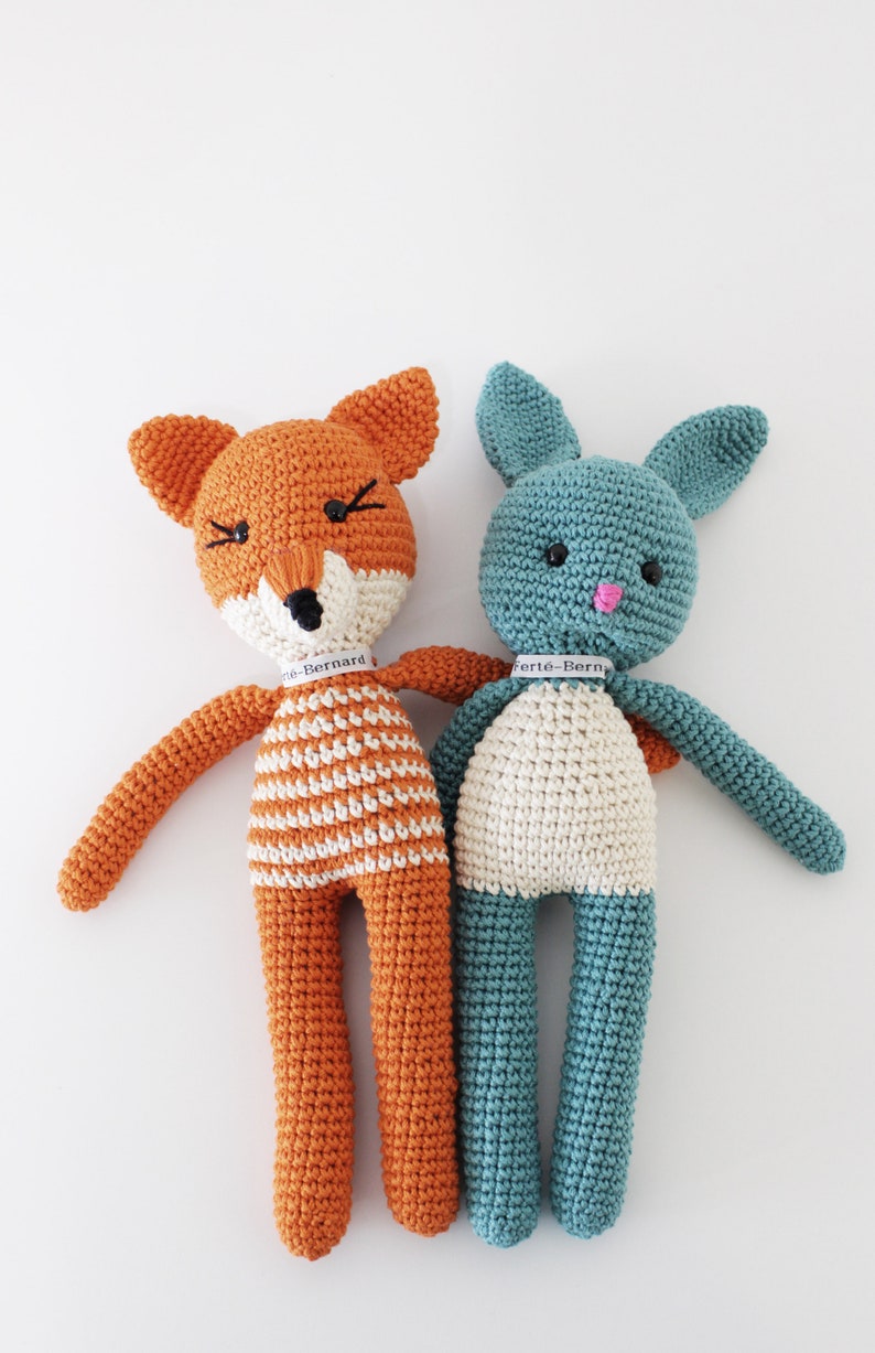 Pode incluir: Dois animais de peluche de croch&ecirc;, uma raposa e um coelho, de p&eacute; lado a lado. A raposa &eacute; laranja com listras brancas e o coelho &eacute; azul turquesa. Ambos t&ecirc;m olhos pretos e narizes cor-de-rosa. A raposa tem uma etiqueta que diz "Berte-Bernard" e o coelho tem uma etiqueta que diz "Berte-Bern".