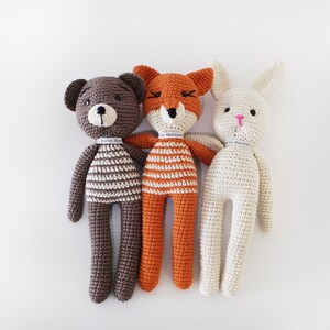 Pode incluir: Tr&ecirc;s animais de peluche de croch&ecirc;: um urso castanho, uma raposa laranja e um coelho branco. Cada animal est&aacute; a usar uma camisa listrada.