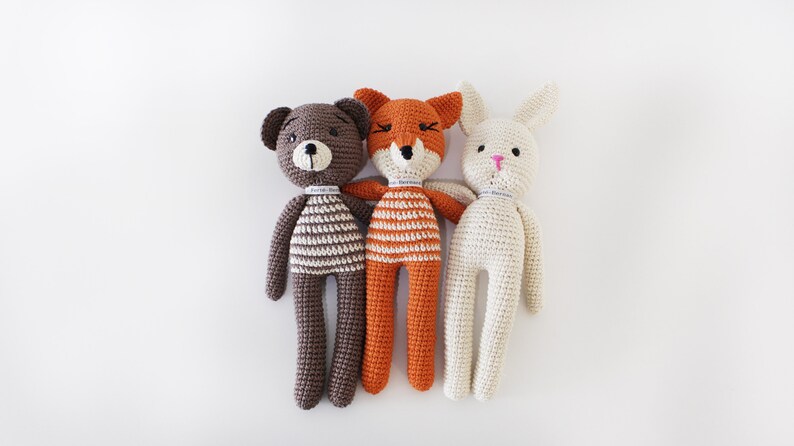 Pode incluir: Tr&ecirc;s animais de peluche de croch&ecirc;: um urso castanho, uma raposa laranja e um coelho branco. Cada animal est&aacute; a usar uma camisa listrada.