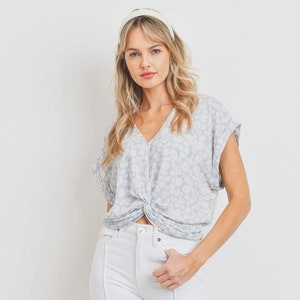 May include: A woman wearing a light blue floral print top with a twist detail at the front, white skinny jeans, and light blue heeled sandals.