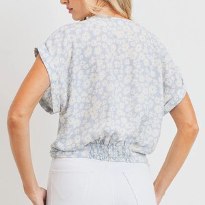 May include: A light blue blouse with a white floral print. The blouse has a gathered elastic waistband and short sleeves.