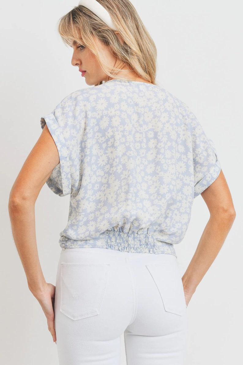 May include: A light blue blouse with a white floral print. The blouse has a gathered elastic waistband and short sleeves.