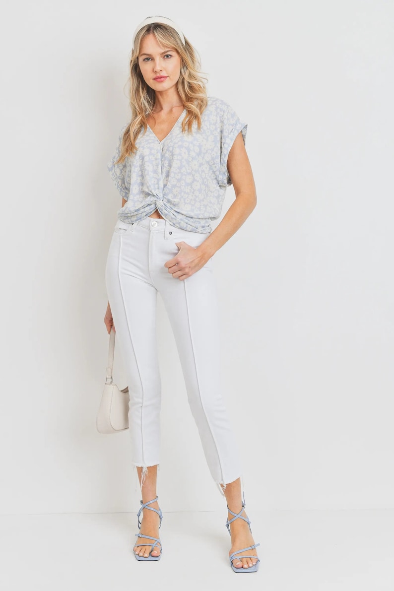 May include: A woman wearing a light blue floral print top with a twist detail at the front, white skinny jeans, and light blue heeled sandals.