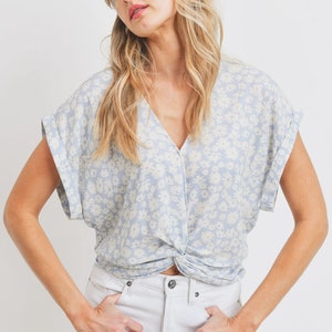 May include: A light blue blouse with a white floral pattern and a twist detail at the front. The blouse has short sleeves and a v-neck.