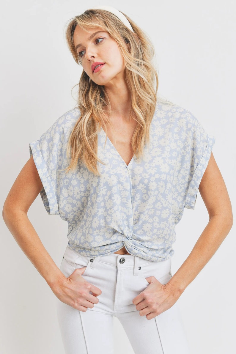 May include: A light blue blouse with a white floral pattern and a twist detail at the front. The blouse has short sleeves and a v-neck.