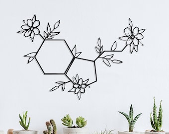 May include: Black metal wall art featuring a stylized floral design with hexagonal shapes. The art is displayed on a white wall above a wooden shelf with potted succulents.