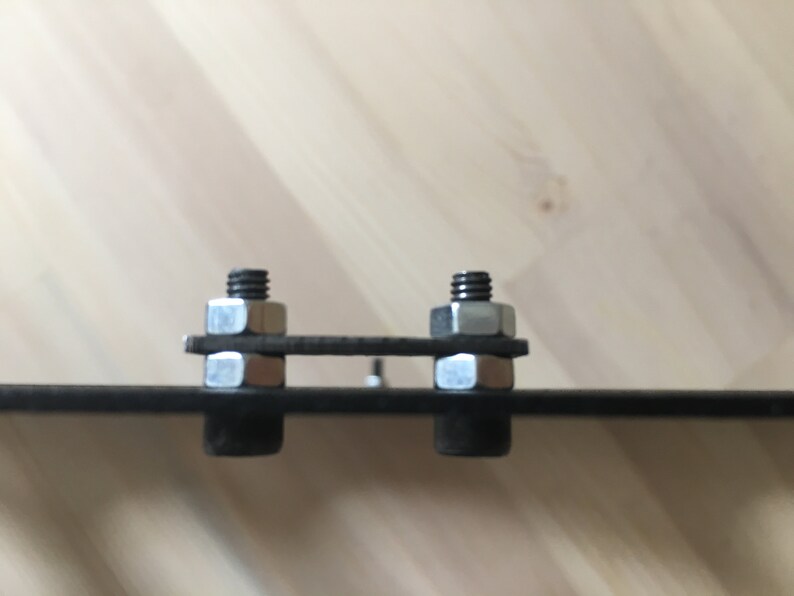 May include: Two silver nuts and bolts are attached to a black metal bar. The nuts and bolts are secured with a washer on each side.