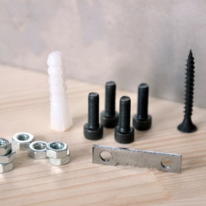 May include: A set of black screws, nuts, and a metal bracket, along with a white plastic anchor. The items are arranged on a light wood surface.