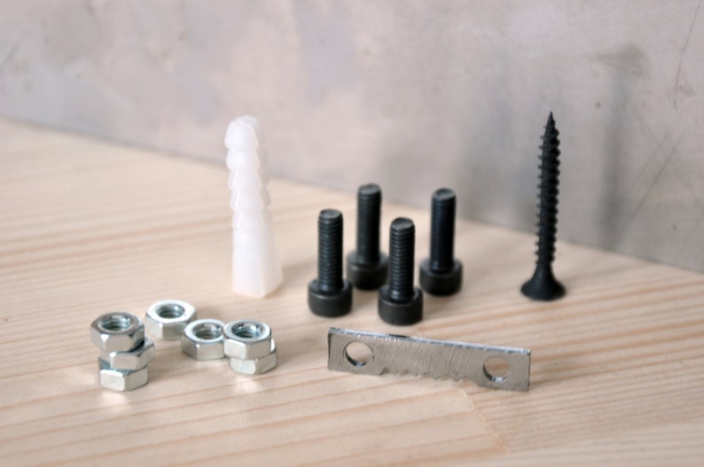 May include: A set of black screws, nuts, and a metal bracket, along with a white plastic anchor. The items are arranged on a light wood surface.