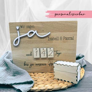 Könnte beinhalten: Ein Holzschild mit den Worten "wir sagen ja" in weißer Schrift, gefolgt von "Isabell & Pascal". Darunter befinden sich drei Holzblöcke mit den Zahlen "142" und dem Wort "Tage" in schwarzer Schrift. Das Schild lautet "noch bis zu unserer Hochzeit" in schwarzer Schrift. Das Schild ist personalisierbar und kann mit verschiedenen Namen und Daten angepasst werden.