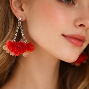 Puede incluir: Pendientes colgantes de cadena plateada con racimos de cuentas rojas y blancas en forma de flor. Los pendientes tienen un aspecto delicado. Las flores son de color rojo vibrante y las cuentas son blancas translúcidas.