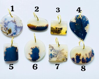 Op de afbeelding: Acht edelsteenhangers met goudkleurige lussen. De hangers variëren in vorm, waaronder rond, ovaal, vierkant en druppelvormig. Elke hanger heeft unieke patronen in tinten wit, blauw, geel en bruin.