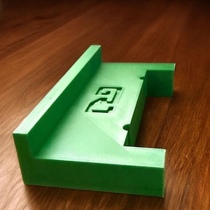 以下が含まれることがあります： 前面に「2」が印刷された緑色のプラスチック製の3Dプリントオブジェクト。オブジェクトは小さなランプまたは棚の形をしています。