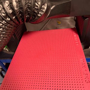 May include: A red perforated mat with a textured surface, labeled "MAX 1.5KG". The mat is part of a larger machine, with a flexible silver duct and other components visible in the background.