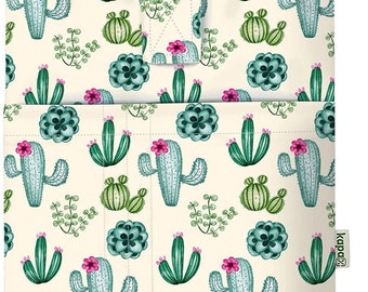 May include: A white reusable shopping bag with a cactus print. The bag has a green, blue, and pink cactus pattern with a small green and brown cactus at the bottom. The bag has a small pocket on the front and a "kapaza" logo on the right side.