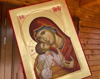 Puede incluir: Un icono pintado a mano de la Virgen María y el niño Jesús. El icono está enmarcado en oro y rojo y tiene las palabras "IC XC" y "MP OY" escritas en él.