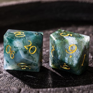 Pu&ograve; includere: Due dadi di pietre preziose con numeri dorati. I dadi hanno un aspetto marmorizzato, con sfumature verdi e blu. I numeri sono ben visibili e i dadi sembrano traslucidi. Questi dadi sono per giochi da tavolo.