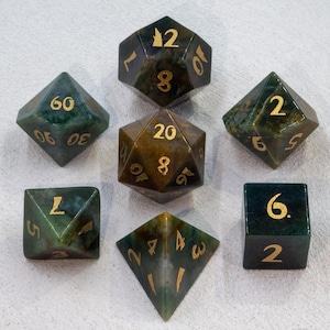 Könnte beinhalten: Satz von sieben grünen und braunen Achatwürfeln mit goldenen Zahlen. Die Würfel sind ein W4, W6, W8, W10, W12 und W20.