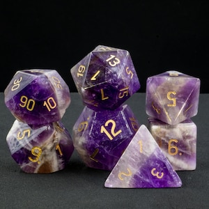 Könnte beinhalten: Sechs Amethyst-Würfel mit goldenen Zahlen. Die Würfel haben verschiedene Formen, darunter ein W4, W6, W8, W10, W12 und W20.