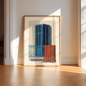 May include: Framed art print featuring a blue window with shutters and a balcony. A striped textile hangs from the balcony. The artwork is set against a cream-colored background and framed in a light wood.