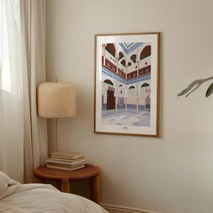 Könnte beinhalten: Ein gerahmter Kunstdruck zeigt einen Innenhof mit gewölbten Türen, detaillierten Balkonen und aufwendigen Fliesenarbeiten. Das Kunstwerk zeigt eine Palette aus Beige, Braun, Blau und Weiß, wodurch ein Gefühl von Tiefe und architektonischen Details entsteht. Der Druck wird an einer neutralfarbenen Wand ausgestellt.