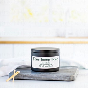May include: Black candle jar with a white label that says "Your Image Here" and "2 Files Included - High Resolution JPEG - PSD with Smart Object". The candle jar is sitting on a gray cutting board with a white towel and matches in the foreground.