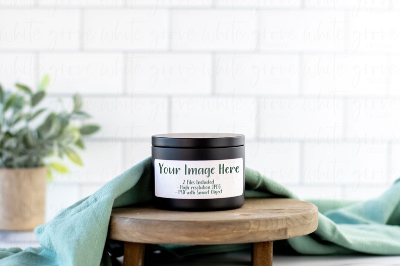 May include: Black candle jar with a white label that says "Your Image Here" and "2 files included: High resolution JPEG, PSD with Smart Object". The candle jar is sitting on a wooden stand with a teal cloth draped over it.