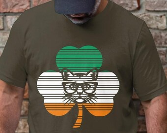 May include: A dark green t-shirt with a white, orange, and green shamrock design. The shamrock has a cat face with glasses in the center.