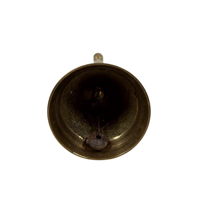 May include: A close-up shot of a brass bell, viewed from the inside. The bell has a rounded shape with a small loop at the top for hanging. The clapper is visible inside the bell. The bell has a shiny, golden appearance.