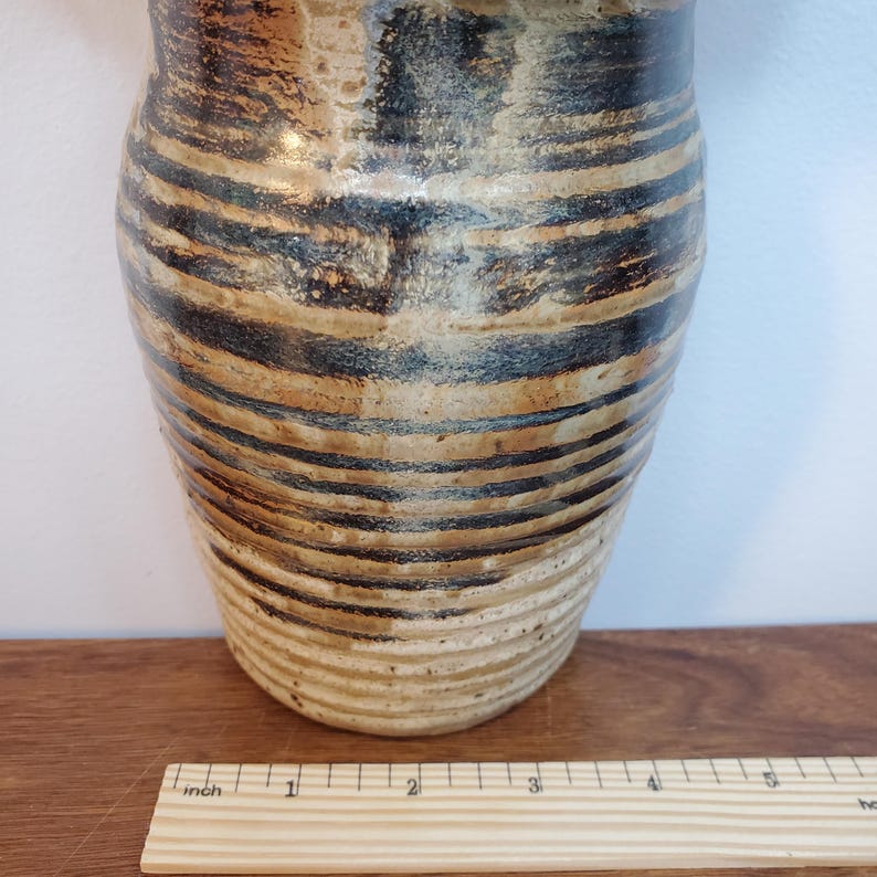 K&ouml;nnte beinhalten: Eine handgefertigte Keramikvase mit zylindrischer Form. Die Vase hat horizontale B&auml;nder in abwechselnden Braun- und Schwarzt&ouml;nen. Die Vase ist etwa 15 cm hoch und hat eine strukturierte Oberfl&auml;che.