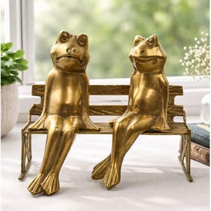 Peut inclure: Deux figurines de grenouilles en laiton sont assises sur un banc décoratif. Les grenouilles ont des détails précis et sont posées comme si elles se détendaient. Le banc a un aspect vieilli et détaillé. L'esthétique générale est vintage et fantaisiste, adaptée à la décoration intérieure.