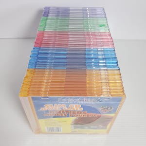Puede incluir: Una pila de fundas delgadas de CD de colores. Las fundas son de varios colores, incluyendo naranja, azul, verde, rosa y morado. El embalaje dice "PerfectMicro Slim CD Jewel Cases" y "50".